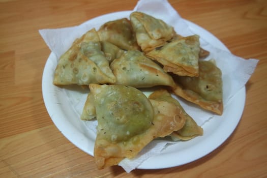 Closeup of delicious home made spicy and crunchy samosa pastries placed in a white ceramic plate on wooden floor