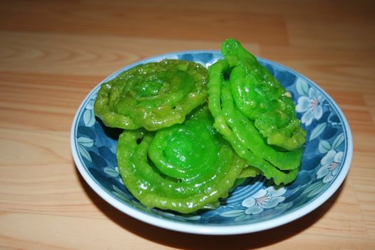 Crispy sweet Asian dessert green Jalebi cooked and served in ceramic plate, Indian sweet street food with juicy syrup, a closeup view.