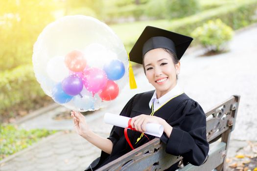 Portrait of happy young female graduates in academic dress and square academic cap holding word quotes of CONGRATS GRAD on balloon after convocation ceremony.