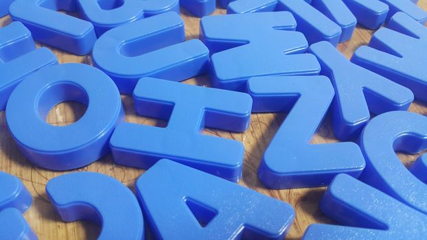 Set of plastic alphabet letters placed on a wooden floor. Alphabet set is used for educating children to learn words and language