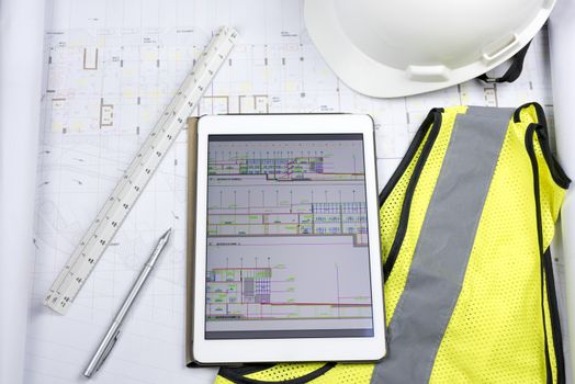 Digital tablet with design drawing, hard copy of drawing, triangular scale ruler and work Personal Protective equipment‎ (safety yellow fluorescent gilet and white helmet)