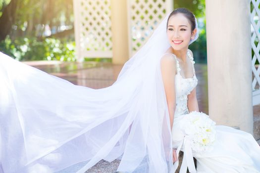 bride is sitting with flowers. Beautiful Young woman posing in park or garden in white bridal dress outdoors on a bright sunny day.