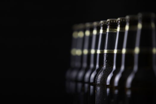 Beer bottles with blank labels lined up in selective focus on black background, one with frost droplets