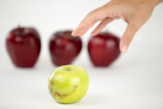 Concept of diversity: a woman's hand is about to grab the only green apple among the other red ones