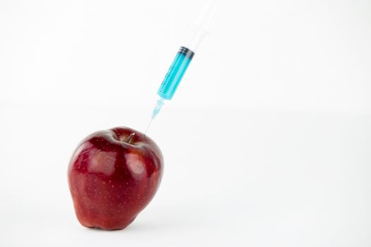 Concept: human GMO manipulation of nature and relative poisoned fruits. Close-up of an apple contaminated with a syringe threaded in and white background