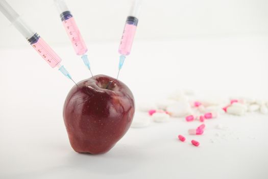 Concept: human GMO manipulation of nature and relative poisoned fruits. Close-up of an apple contaminated with three syringe threaded in and medicines on a white background