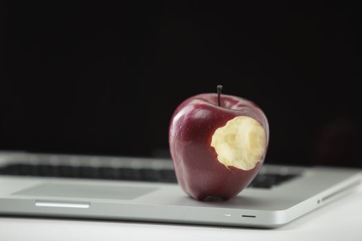 Shiny red apple resting on an open aluminum laptop in selective focus on white background