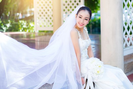 bride is sitting with flowers. Beautiful Young woman posing in park or garden in white bridal dress outdoors on a bright sunny day.
