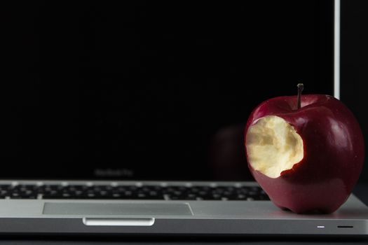 Shiny red apple resting on an open aluminum laptop in selective focus on a black background