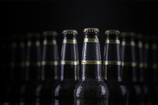 Beer bottles with blank labels lined up in selective focus on black background, one with frost droplets