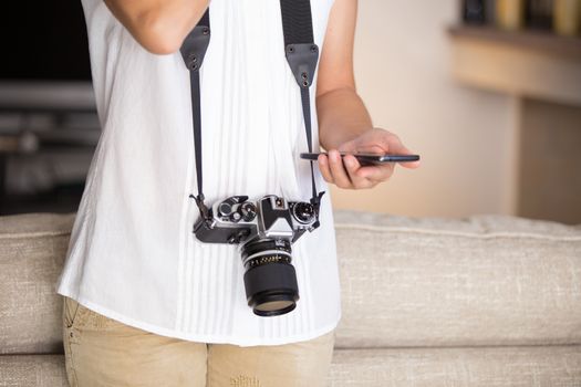 Contrast between old and modern times: a young woman with a vintage camera around her neck fiddles with her smartphone