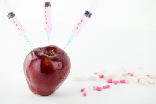 Concept: human GMO manipulation of nature and relative poisoned fruits. Close-up of an apple contaminated with three syringe threaded in and medicines on a white background