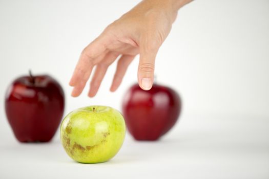 Concept of diversity: a woman's hand is about to grab the only green apple among the other red ones