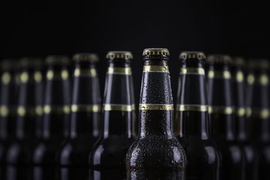 Beer bottles with blank labels lined up in selective focus on black background, one with frost droplets