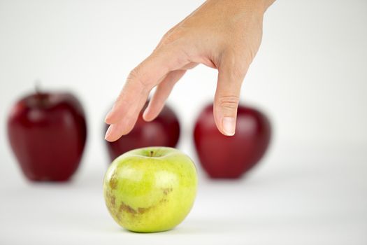 Concept of diversity: a woman's hand is about to grab the only green apple among the other red ones