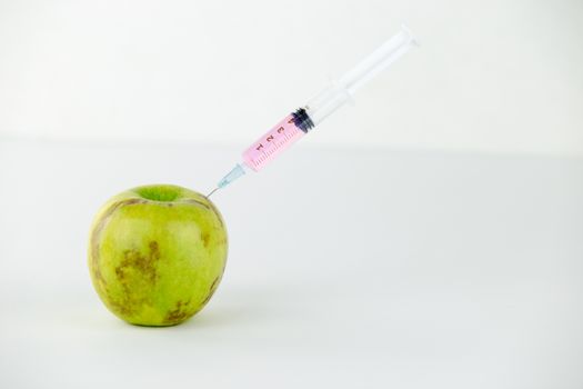 Concept: human GMO manipulation of nature and relative poisoned fruits. Close-up of an apple contaminated with a syringe threaded in and white background