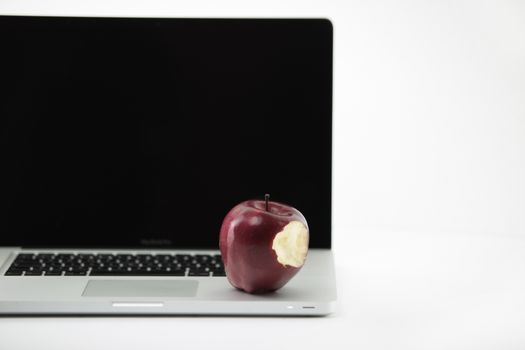 Shiny red apple resting on an open aluminum laptop in selective focus on a black background