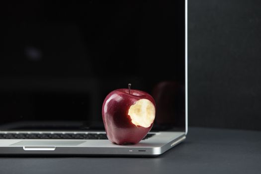 Shiny red apple resting on an open aluminum laptop in selective focus on a black background