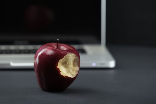 Shiny red apple resting on an open aluminum laptop in selective focus on a black background