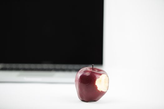 Shiny red apple resting on an open aluminum laptop in selective focus on white background