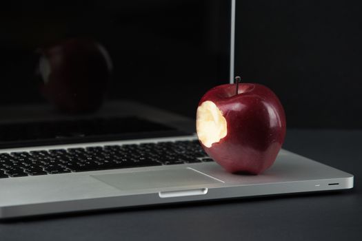 Shiny red apple resting on an open aluminum laptop in selective focus on a black background