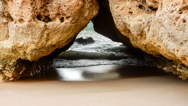 Detail of the cliffs in the Algarve, Portugal, the rocks form a small arc on the sand bathed by the ocean