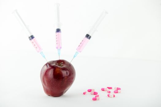 Concept: human GMO manipulation of nature and relative poisoned fruits. Close-up of an apple contaminated with three syringe threaded in and medicines on a white background