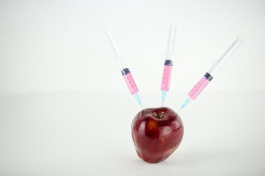 Concept: human GMO manipulation of nature and relative poisoned fruits. Close-up of an apple contaminated with three syringes threaded in and white background