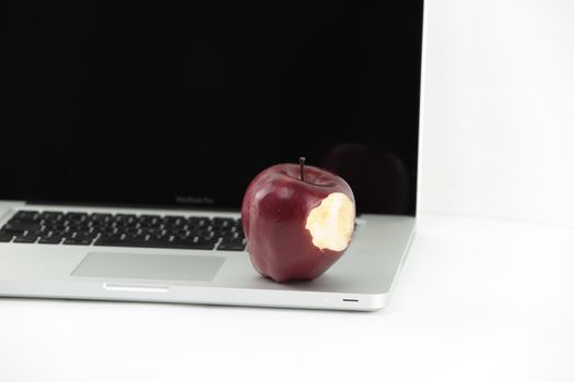 Shiny red apple resting on an open aluminum laptop in selective focus on white background