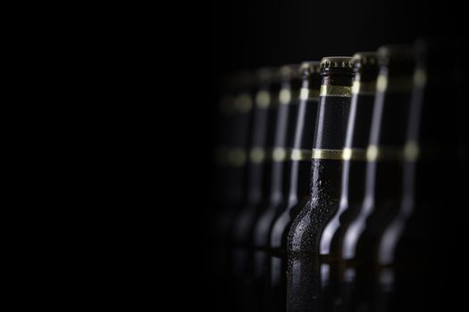 Beer bottles with blank labels lined up in selective focus on black background, one with frost droplets