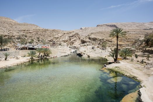 Tourists around Main pool of Wadi Bani Khalid with some going and coming back from the canyon where you can go to see the cave, Oman