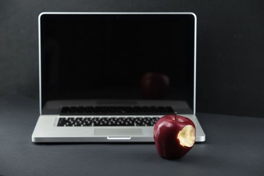 Shiny red apple resting on an open aluminum laptop in selective focus on a black background