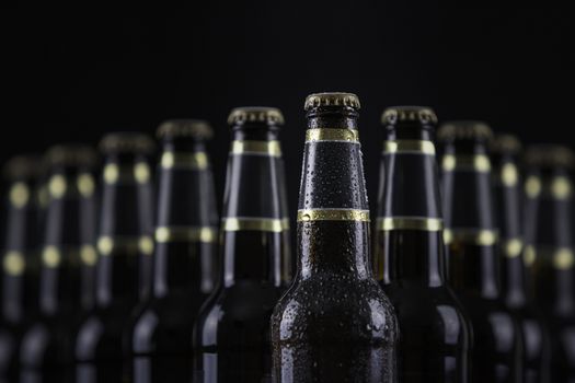 Beer bottles with blank labels lined up in selective focus on black background, one with frost droplets
