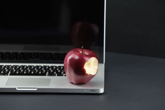 Shiny red apple resting on an open aluminum laptop in selective focus on a black background