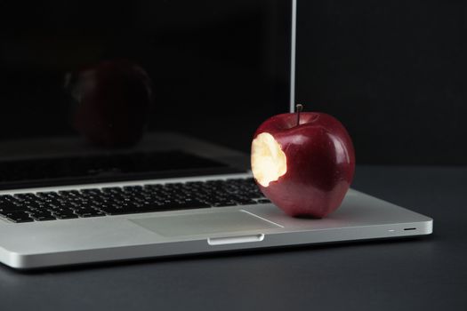 Shiny red apple resting on an open aluminum laptop in selective focus on a black background