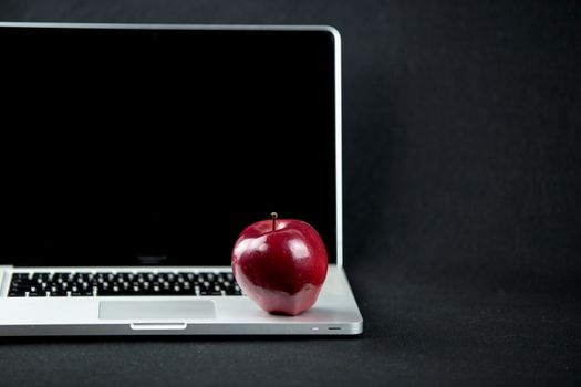 Shiny red apple resting on an open aluminum laptop in selective focus on a black background