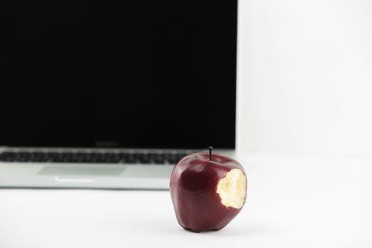 Shiny red apple resting on an open aluminum laptop in selective focus on white background