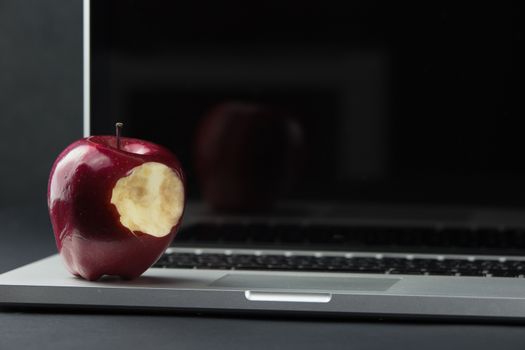 Shiny red apple resting on an open aluminum laptop in selective focus on a black background