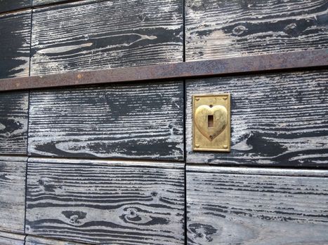Concept: love never gets old. An old wooden door discolored by time with the heart-shaped brass lock