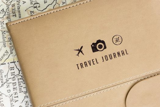 Close-up of a Travel Journal cover with 3 small logos (a plane, a camera and a compass) and a ancient map at background.