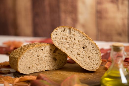 Autumnal rustic food: a whole loaf cut in half on an old wooden cutting board, ampoule of extra virgin olive oil and red and orange wisteria leaves around