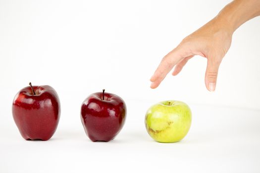 Concept of diversity: a woman's hand is about to grab the only green apple among the other red ones