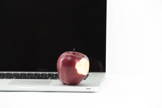 Shiny red apple resting on an open aluminum laptop in selective focus on a black background