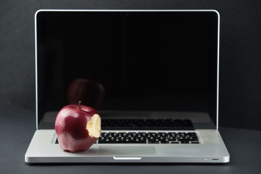 Shiny red apple resting on an open aluminum laptop in selective focus on a black background