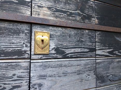 Concept: the key to open the heart. An old wooden door discolored by time with the heart-shaped brass lock