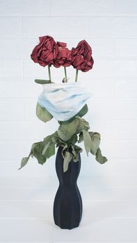 Three wilted roses in a medical mask as a symbol of the covid pandemic.Flowers are quarantined in a protective mask against viruses,colds and flu.Preventing the development of an outbreak of infection