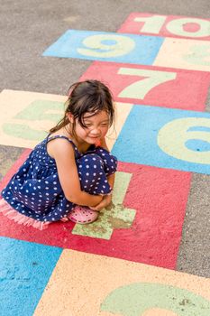Young girl playing hopscotch on playground with happiness.