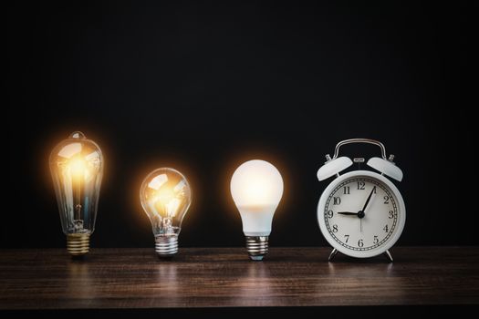 light bulb with white alarm clock on wood table on black background, time to innovation and idea to success conccept