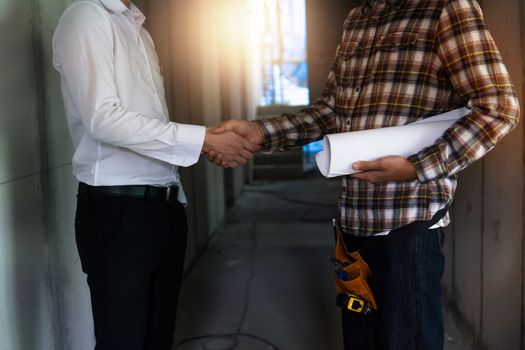 engineer worker holding blueprint shake hand with house agent  in construction site 