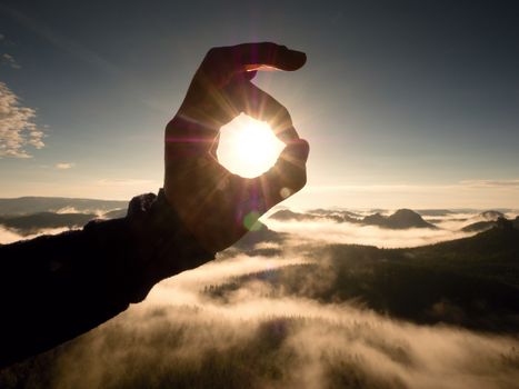 Man hand touch Sun. Misty daybreak in a beautiful hills. Peaks of hills are sticking out from foggy background, the fog is red and orange due to Sun rays. Lens defects.